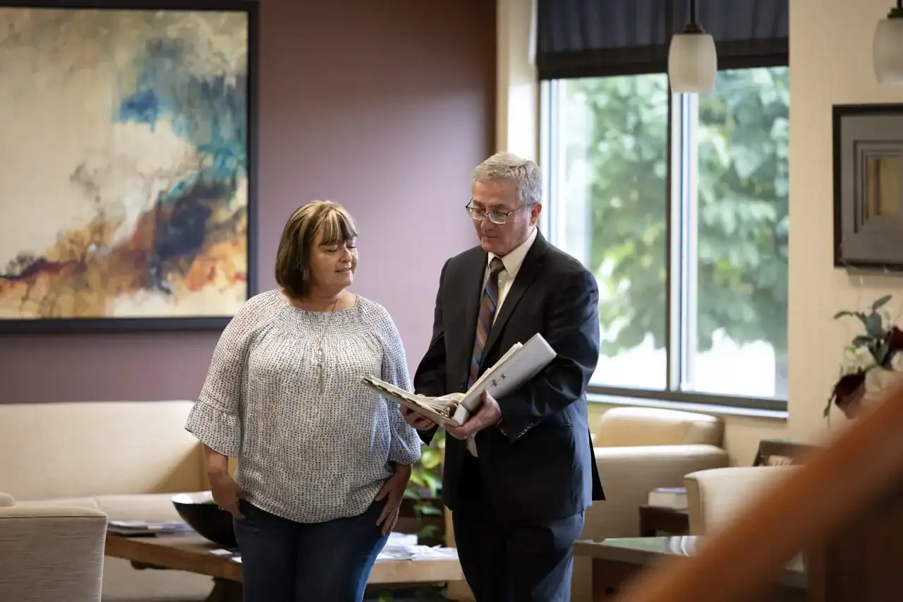 A professional man in a suit discusses documents with a woman in a casual blouse in a well-lit, modern office. They appear to be engaged in a serious conversation, possibly about career advice or planning.