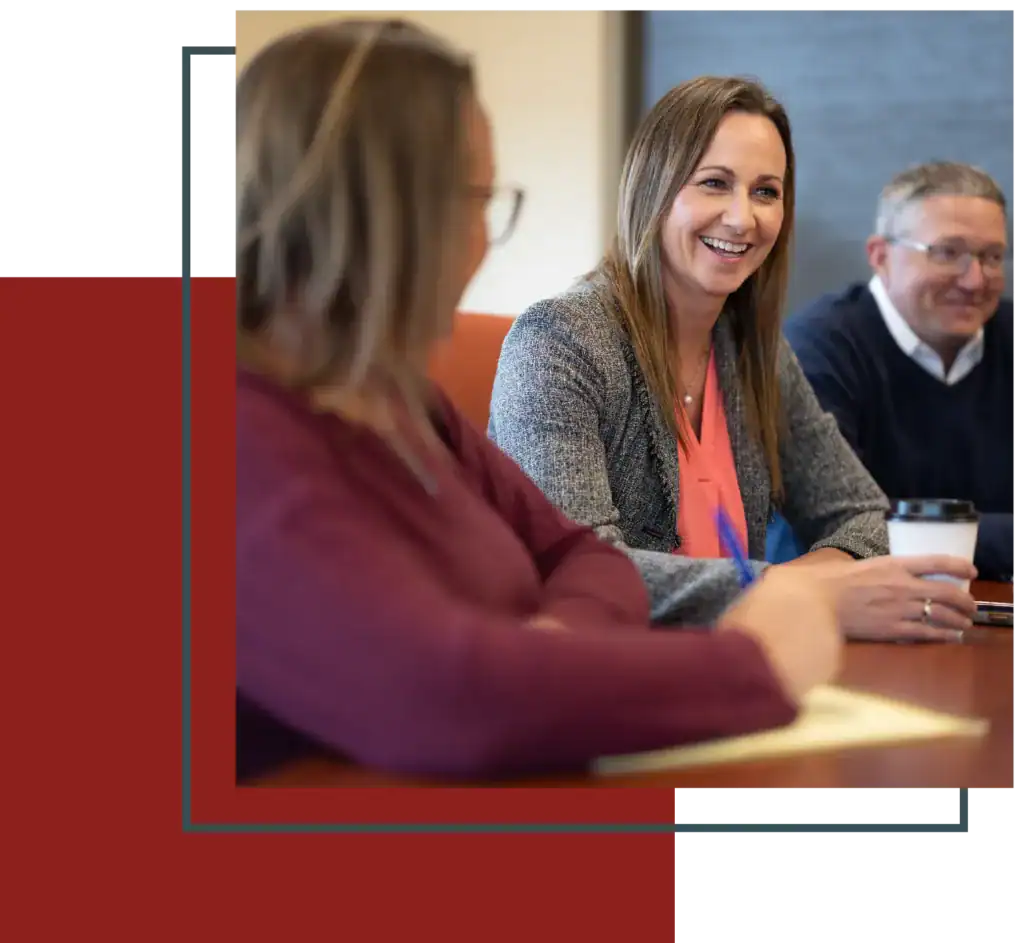An engaged woman in a blazer smiling while participating in a business meeting with colleagues in a conference room.